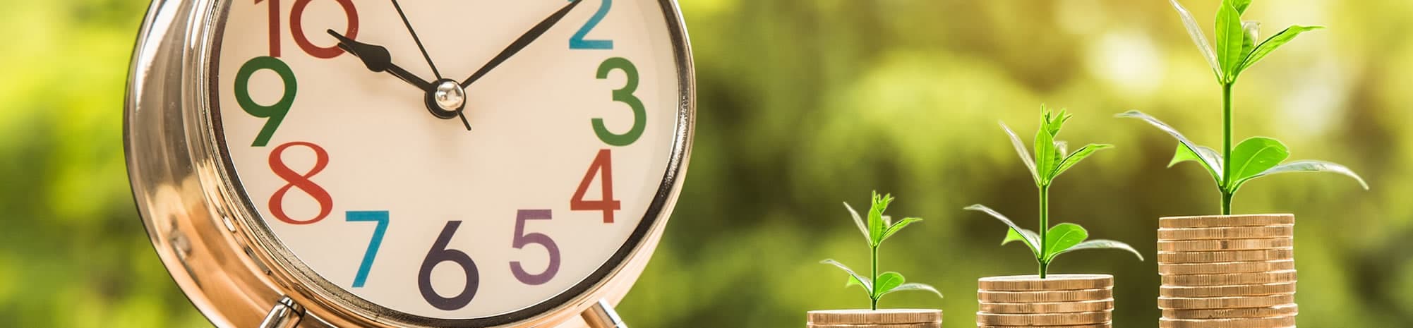 An alarm clock beside seedlings growing from stacks of coins